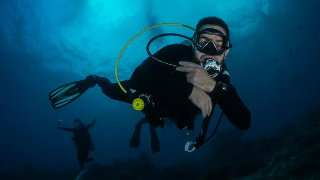 Scuba diver in full gear swimming underwater in deep blue ocean water
