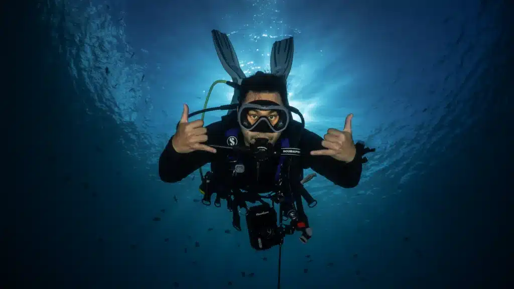 Scuba diver underwater making shaka hand signs with sunlight beaming from above