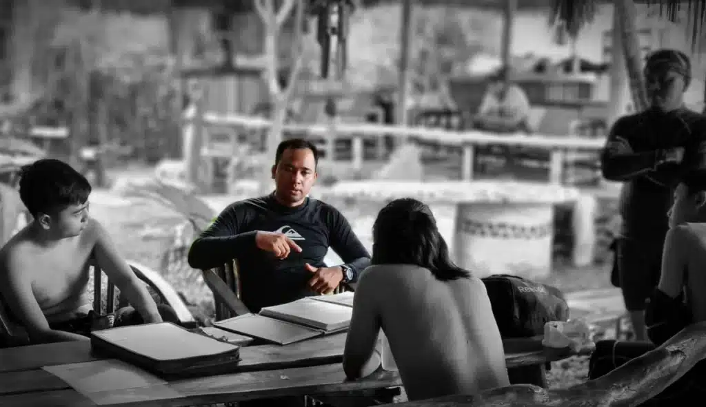 An instructor speaking to a group of students seated around an outdoor table